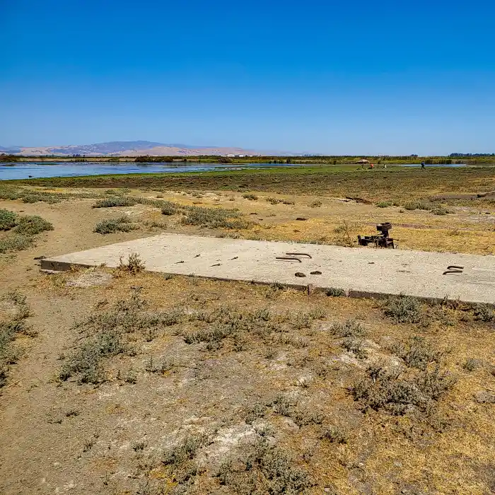 A small concrete pad in an arid area, with marsh and open water in the background.